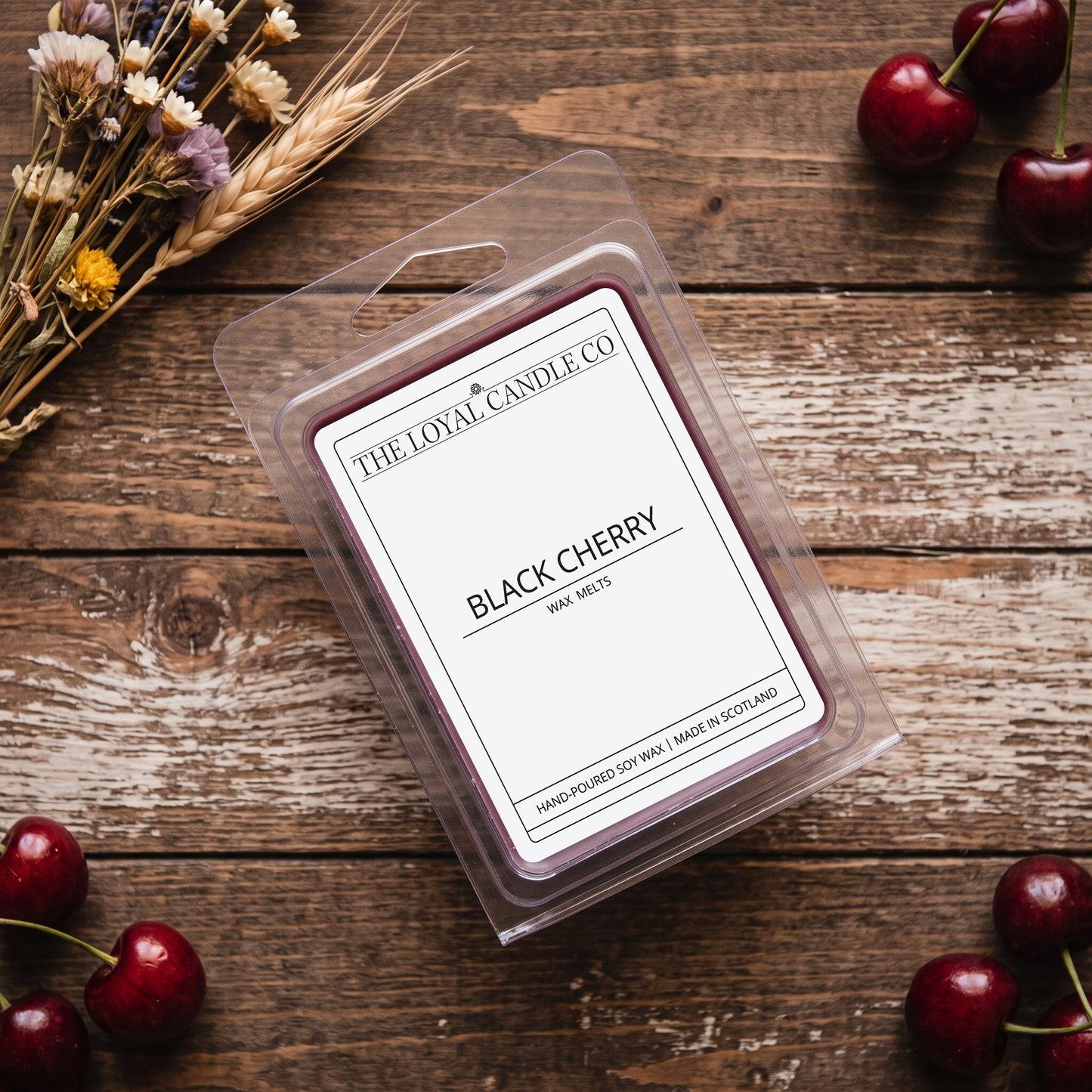 Black Cherry wax melt clamshell on a dark wood background with dried wheat sprigs