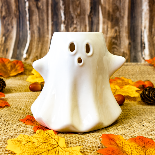 White ghost shaped wax melter on a rustic background with autumn leaves and pinecones.