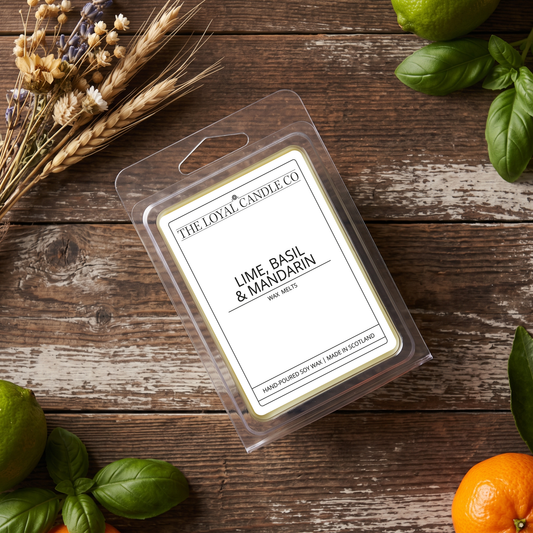  Lime, Basil & Mandarin wax melt clamshell with fresh limes on a dark wood background.